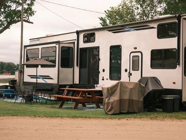 Parked camper trailer with outdoor picnic setup and covered grill.