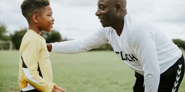 Coach encouraging a young soccer player during practice outdoors.