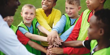 Children and coach join hands in a team huddle on a soccer field.