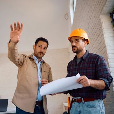 Two men discussing construction plans indoors, one wearing a hard hat.