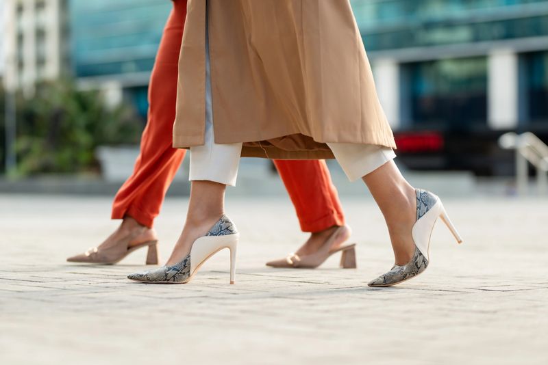 Close-up shot of two businesswomen in stylish heels walking outdoors in a professional environment, representing confidence, entrepreneurship, and modern fashion sense in a bustling urban setting.