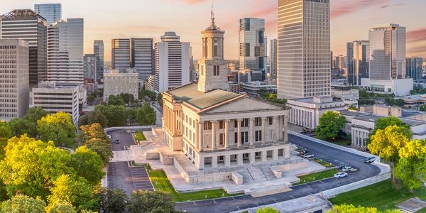 Historic building in front of modern city skyline at sunset.