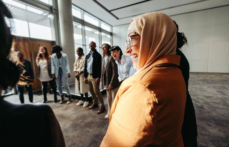 A diverse team engages in a bonding activity, with a Muslim woman laughing in a circle during a workshop.