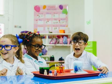 Three kids in lab coats and glasses excited by a colorful science experiment.