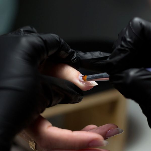 Close-up of a nail technician applying polish with a brush on a client's fingernail.