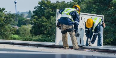 Two construction workers in safety gear working on a rooftop installation.