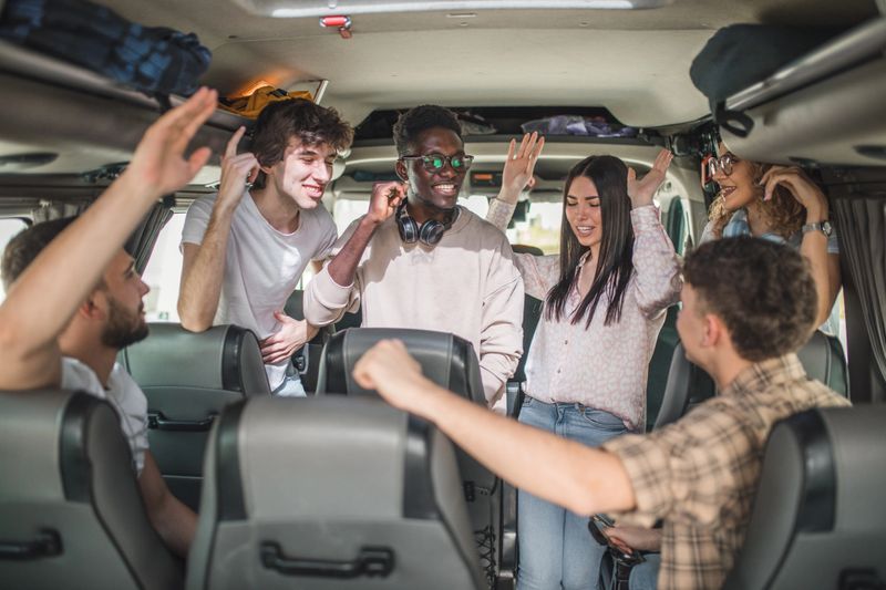 A multiracial group of cheerful friends singing and dancing while riding a bus on a field trip
