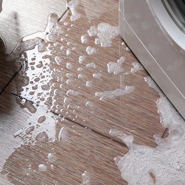 Soapy water spilled on wooden floor near washing machine.