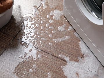 Soapy water spilled on the floor next to a washing machine.