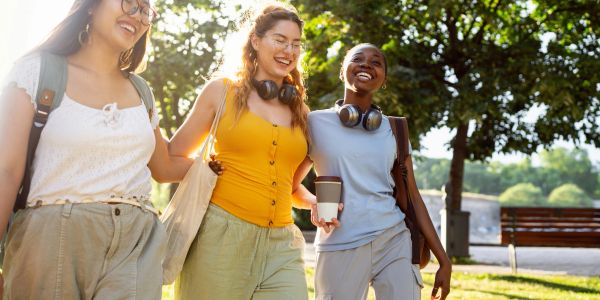 Three friends walking happily outdoors on a sunny day.