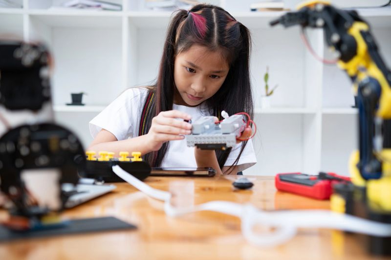 Young girl with pigtails working on assembling a robot with various parts on the table, focused and engaged.