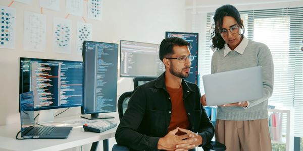 Two software developers reviewing code on a laptop in a modern office.