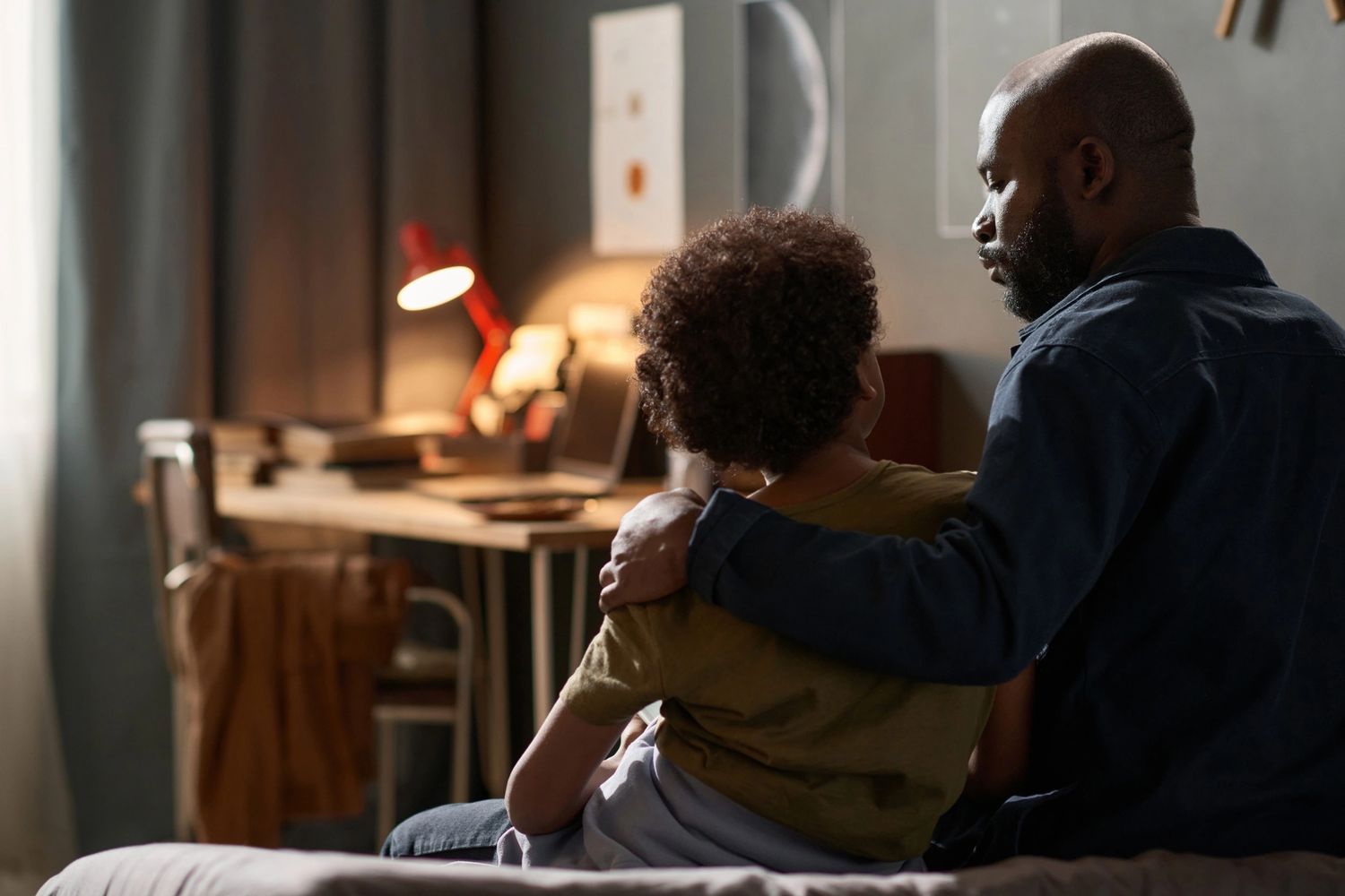 A father comforts his child in a cozy, softly lit room.