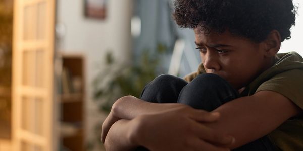 Boy sitting holding knees looking upset.