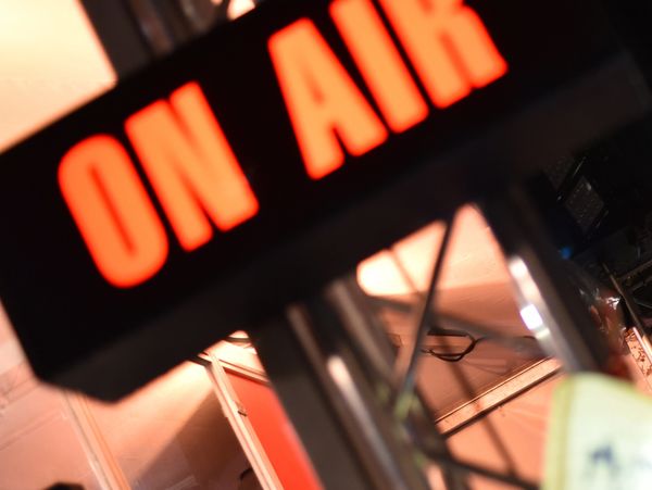 Bright red "ON AIR" sign glowing in a dimly lit studio environment.