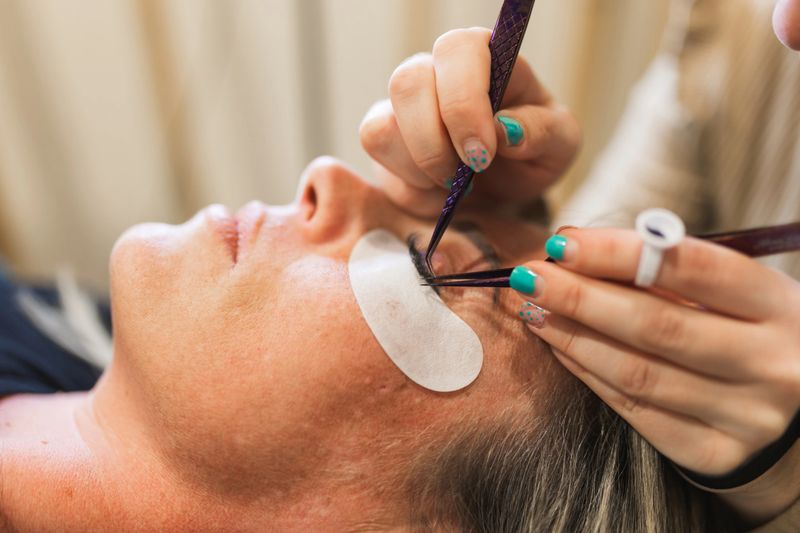 Skilled makeup artist meticulously applying false eyelashes to a client. The artists poised hand wields the lashes with precision, enhancing the clients features.