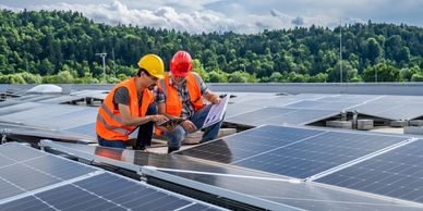 Two workers inspecting solar panels on a rooftop with a forest backdrop.