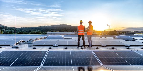 Two workers inspect solar panels on a rooftop at sunset.