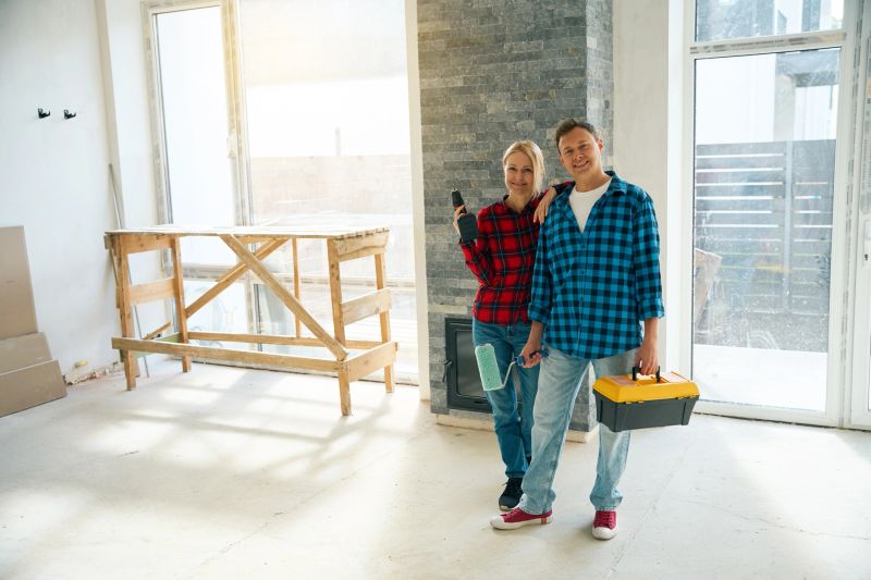 Contented couple standing in room when man holding tool box and paint roller in hands while woman holding electric screwdriver