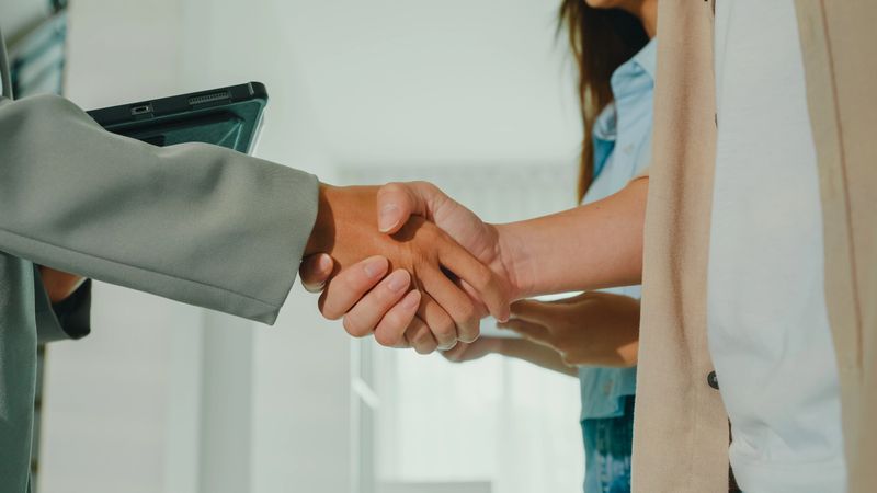 Close-up of Asian female real estate agent handshaking after complete agreement with tenants after showing new houses. Landlord selling real estate to happy couple customer for investment concept.