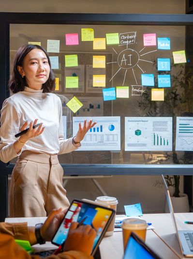 A woman presents AI-related ideas on a glass board to colleagues in a meeting room.