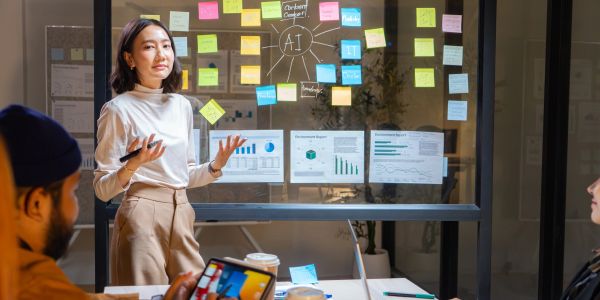 Woman presenting AI strategy with sticky notes and charts on glass board in a meeting.