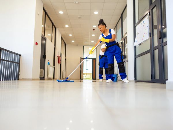 Two janitors cleaning a hallway floor with mops.