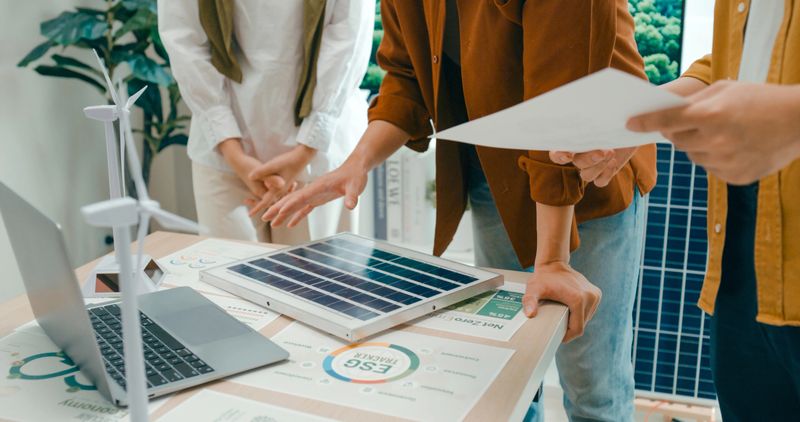 Closeup of diverse team business meeting gathers around laptop in office to discuss sustainable design options involving solar and wind energy. Eco-Friendly Business Team Discussing ESG Goals concept.