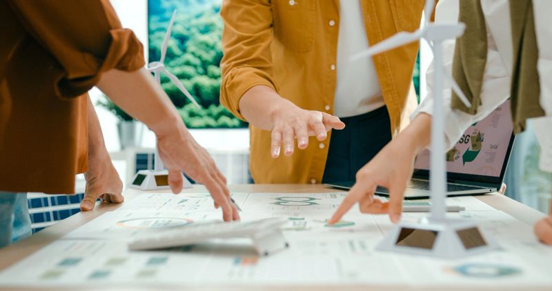 Closeup of team members examine ESG-related documents, pointing and discussing investment strategies for sustainable and renewable energy resources. Eco-Friendly Business Discussing ESG Goals concept.