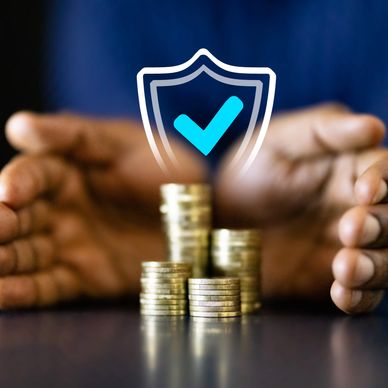 Hands protecting stacked coins with a shield and checkmark symbol.