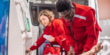 Paramedics in red uniforms attending to an injured man in an ambulance.