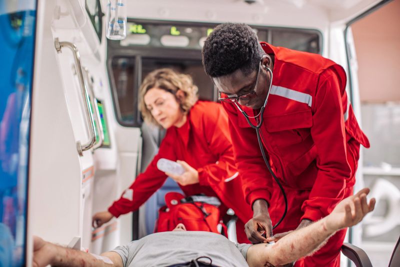 Paramedic is taking the blood pressure of an injured patient while his colleague is preparing medical equipment