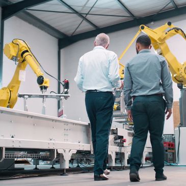 Two men observing industrial robots in a factory.