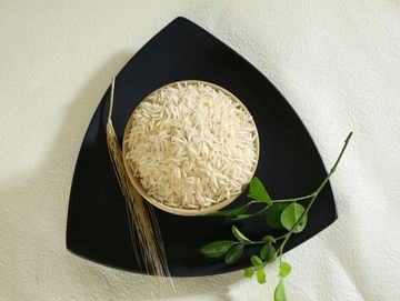 Bowl of raw rice, wheat stalk, and green leaves on a black triangular plate.