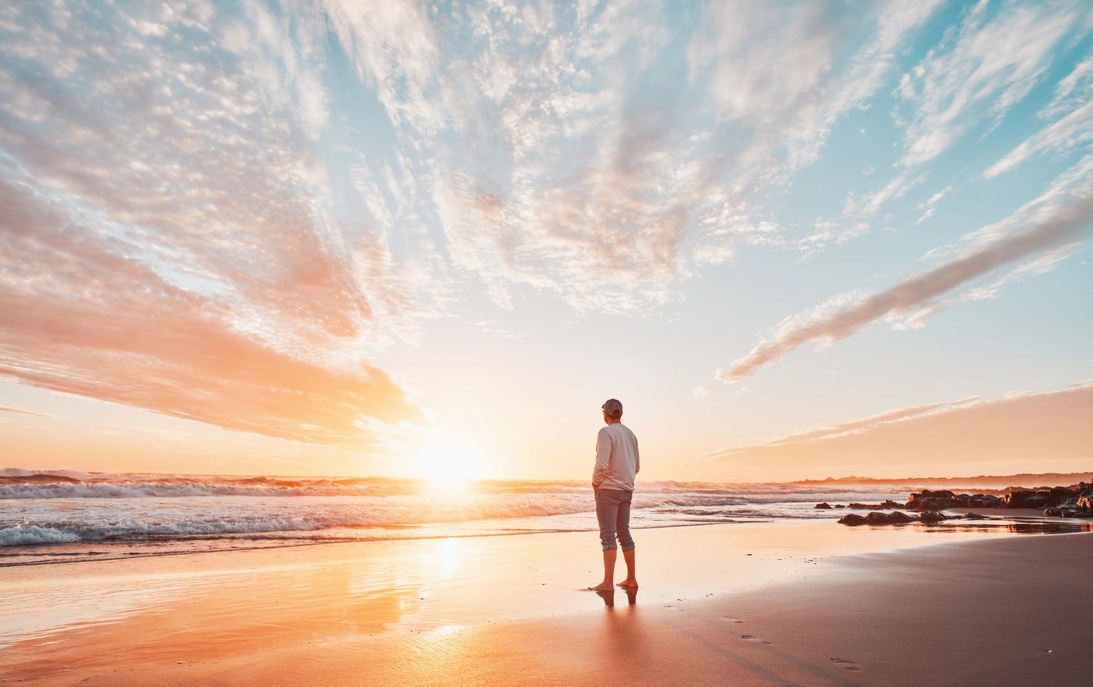 A person watching a serene sunrise on the beach with soft waves.