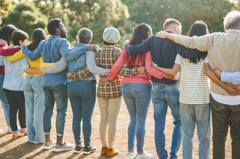 Group of multiracial people hugging each other at city park - Back view of multi generational community outdoor - Humanity concept