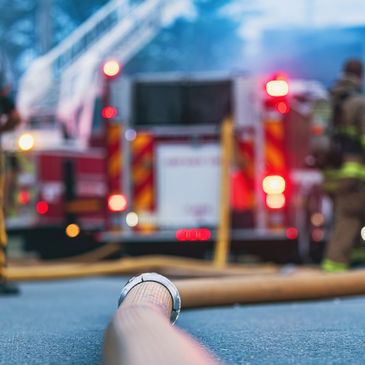 Firefighters and police at an active fire scene with hoses on the ground.
