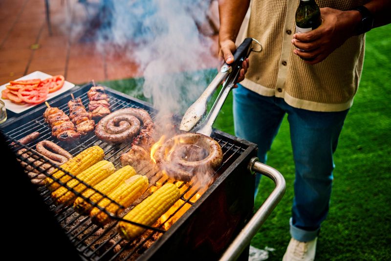 Close-up of grilling sausages and corn on an outdoor barbecue. Social gathering with food. Summer cooking and celebration concept.