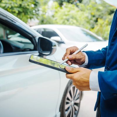 A person in a blue suit uses a stylus on a tablet in front of a white car