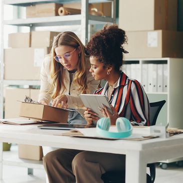 Two women collaborating on work in an office with documents and a tablet.