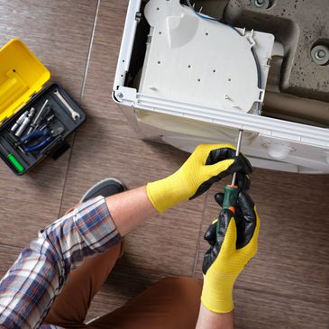 Person repairing a washing machine with tools and wearing yellow gloves.