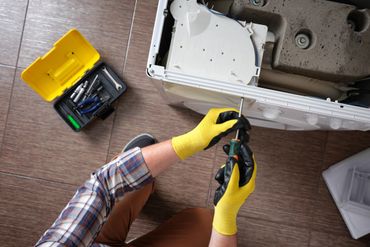Person repairing a washing machine with tools and wearing yellow gloves.