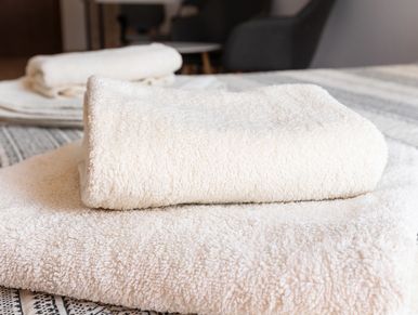 Two neatly folded white towels on a bed with a striped cover.