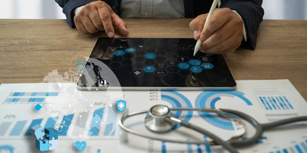Healthcare professional analyzing revenue cycle reports on iPad with printed data and stethoscope.