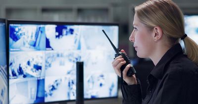 Security officer monitoring surveillance footage holding a walkie-talkie.