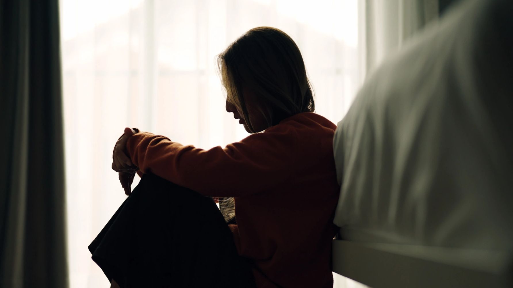Silhouette of a woman sitting on the floor, appearing reflective or sad.