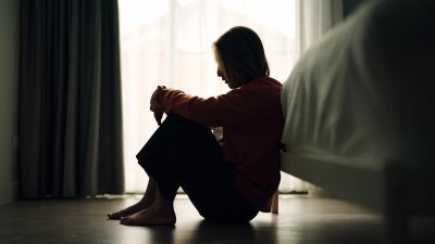 A person sitting on the floor in silhouette near a bed.
