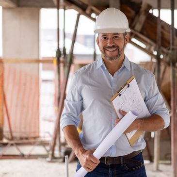 Smiling construction engineer holding blueprints at a building site.