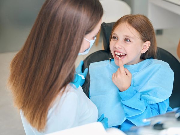 Child pointing at her teeth at the dentist.