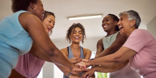 Group of diverse women stacking hands in a team huddle, smiling.